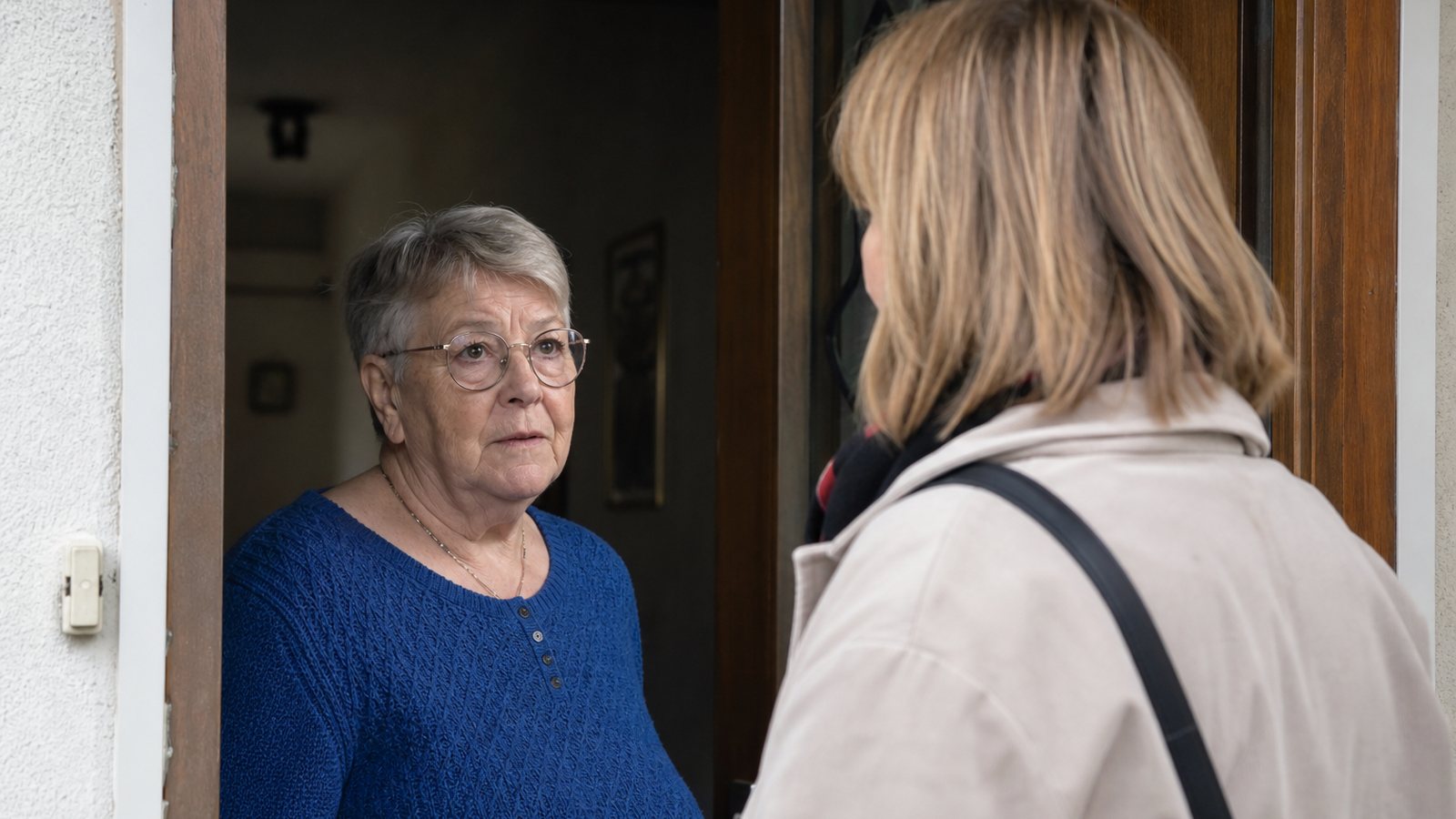 Aide à domicile échangeant avec la fille d'une personne âgée devant la porte du logement